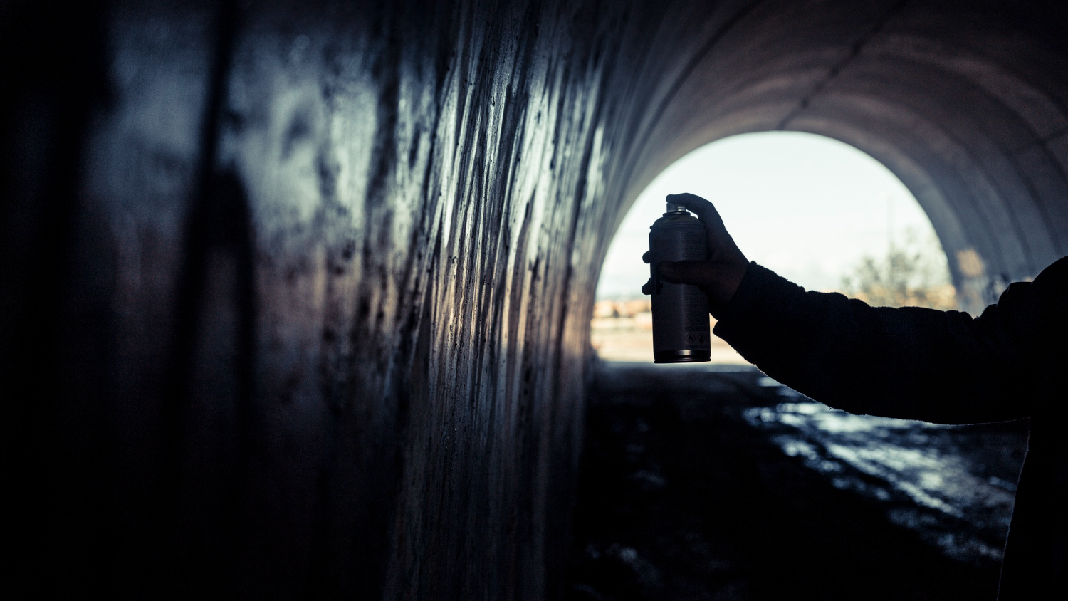 artist hand painting graffiti with spray can inside tunnel