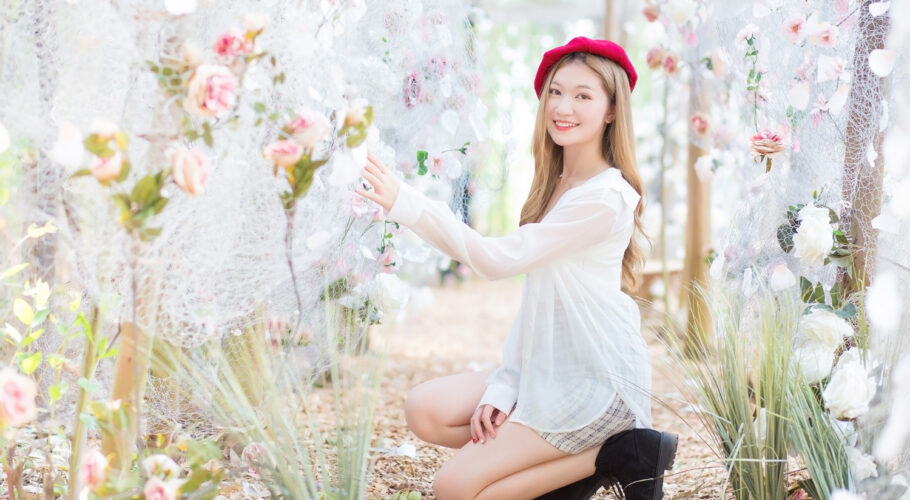 beautiful asian woman crouching down in white dress and black boots wearing red cap