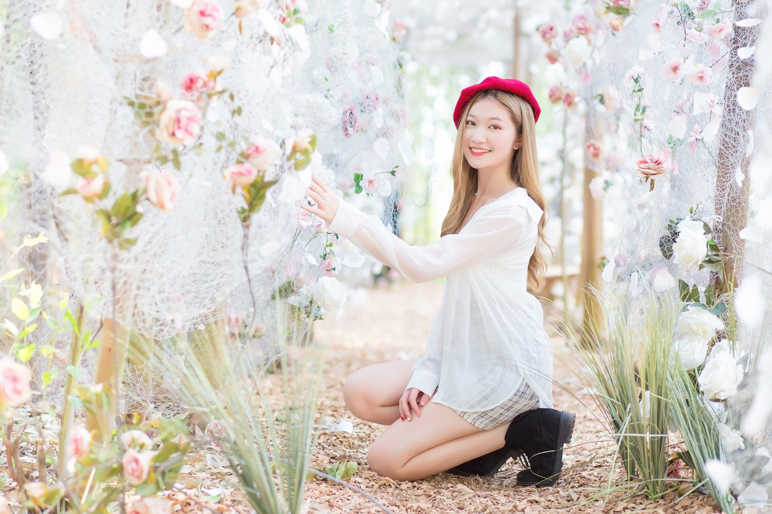 beautiful asian woman crouching down in white dress and black boots wearing red cap