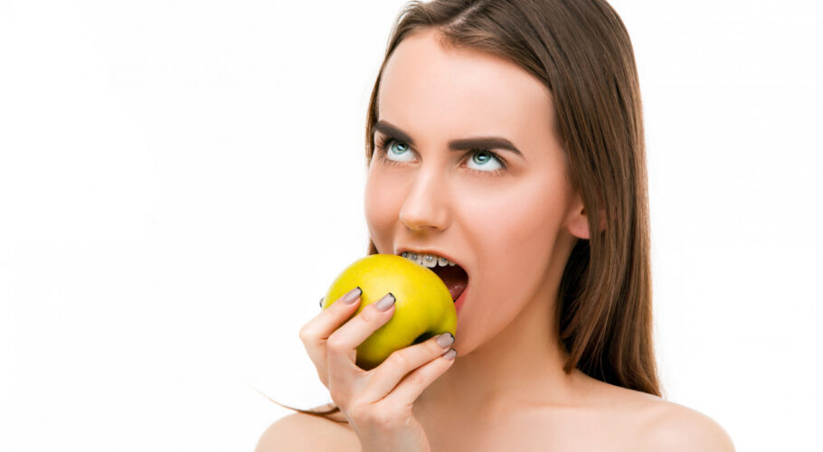 beautiful young woman tabitha with braces on teeth biting apple