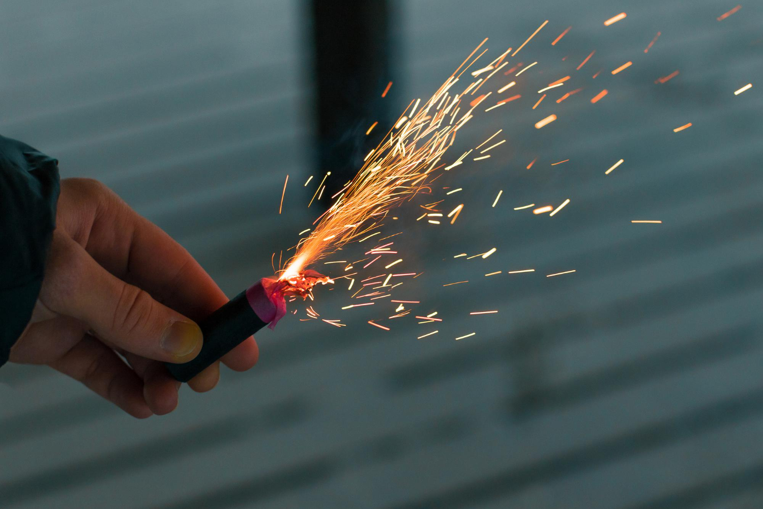 a guy holding a burning a firecracker with sparks