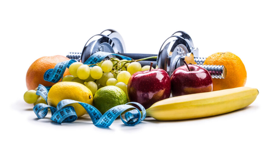 chrome dumbbells surrounded with healthy fruits and measuring tape