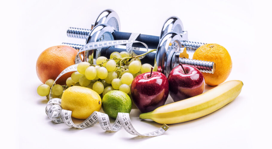 chrome dumbbells surrounded with healthy fruits and measuring tape calorie diet