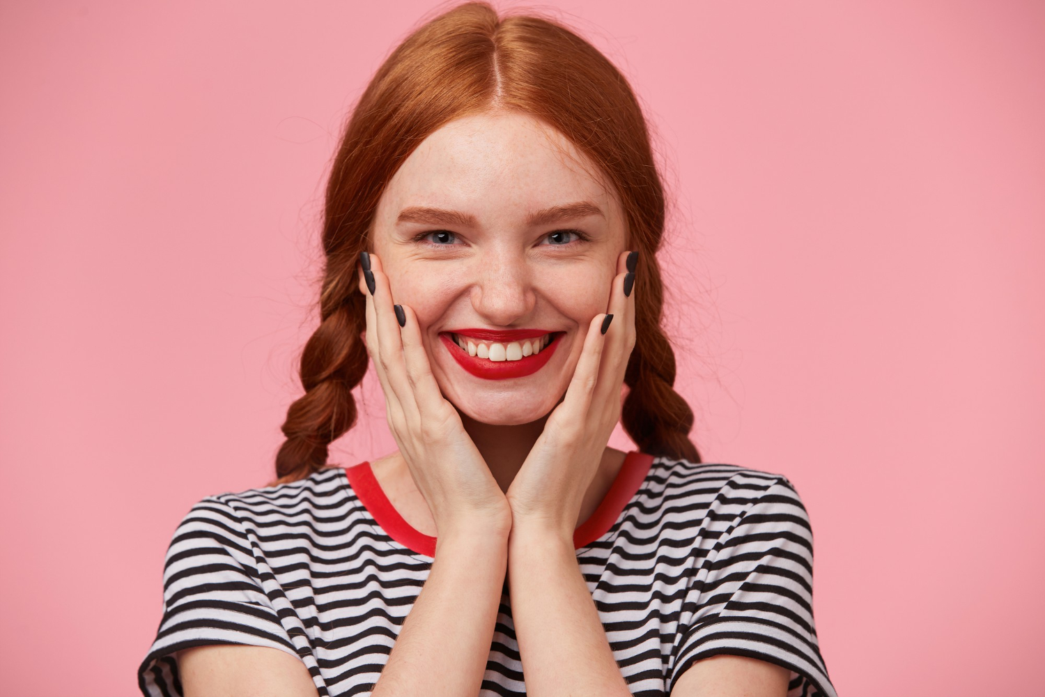 close up glad joyful beautiful red haired girl with two braids keeps hands near her face smiling rosily