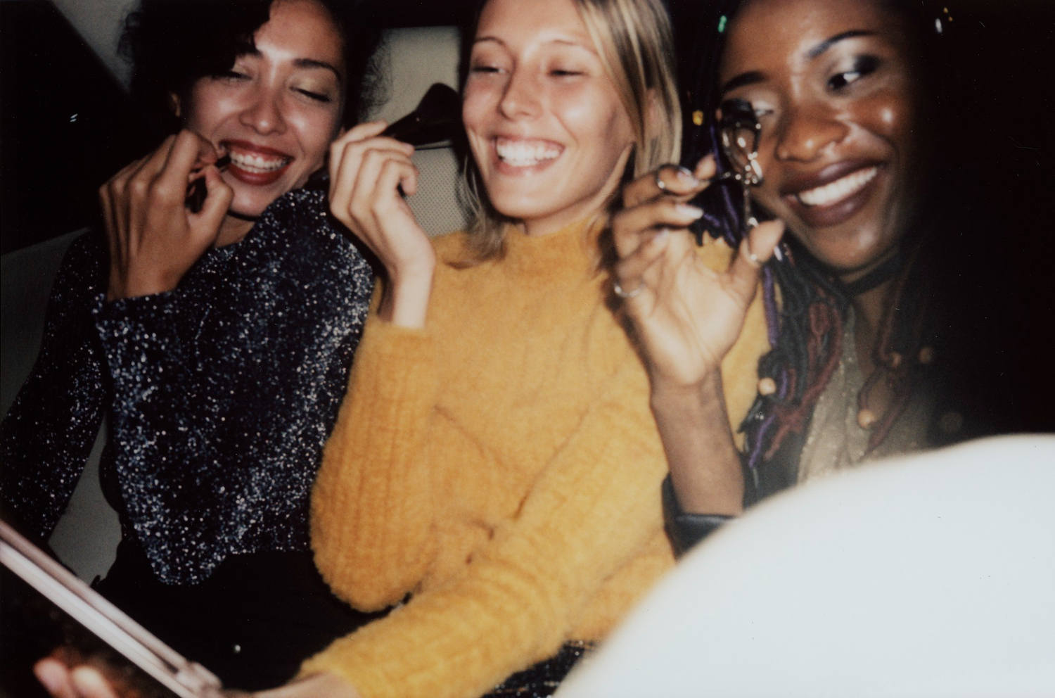 three girls in backseat driving to birthday party putting makeup on and laughing