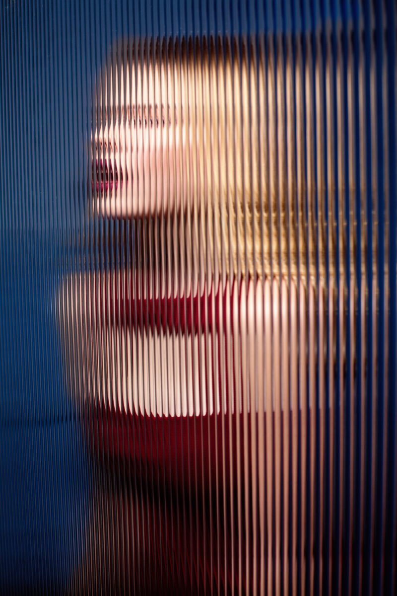 blonde fashion model jewell with red dress and lipstick behind striped corrugated glass
