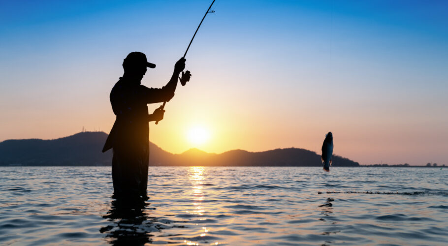 fisherman throwing his rod into a fishing lake with beautiful morning sunset