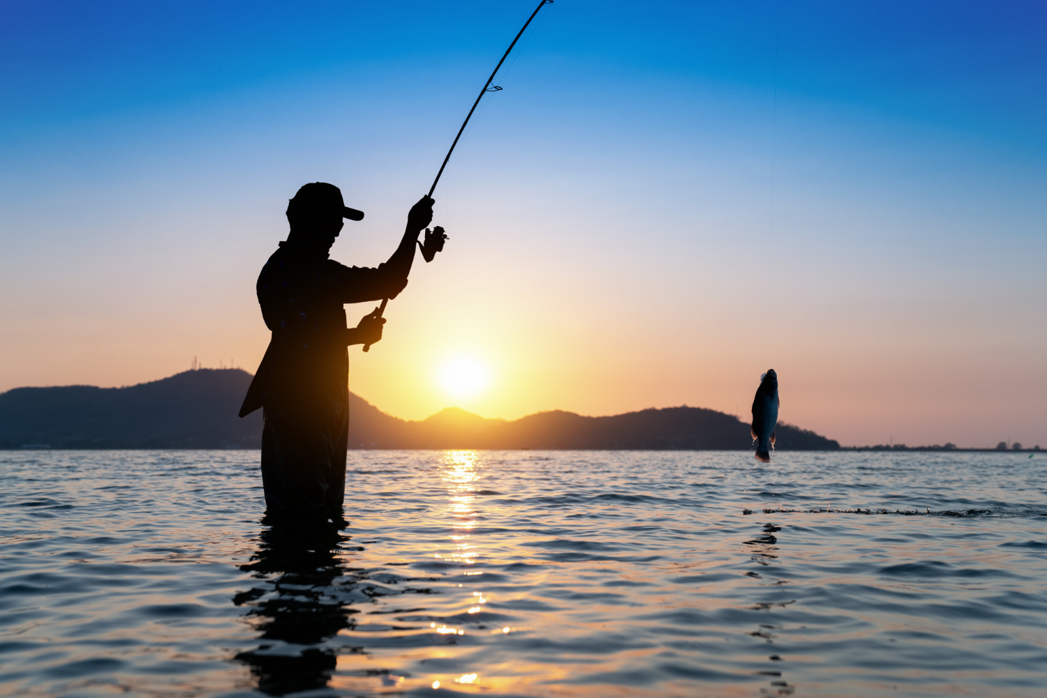 fisherman throwing his rod into a fishing lake with beautiful morning sunset