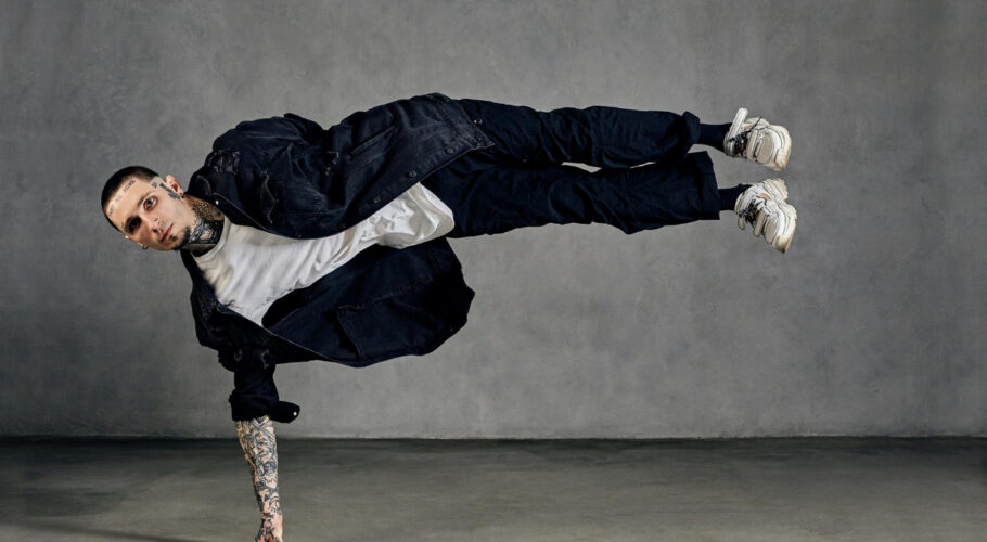 flexible fellow with tattooed body face earrings beard dressed white tshirt sneakers black denim shirt pants