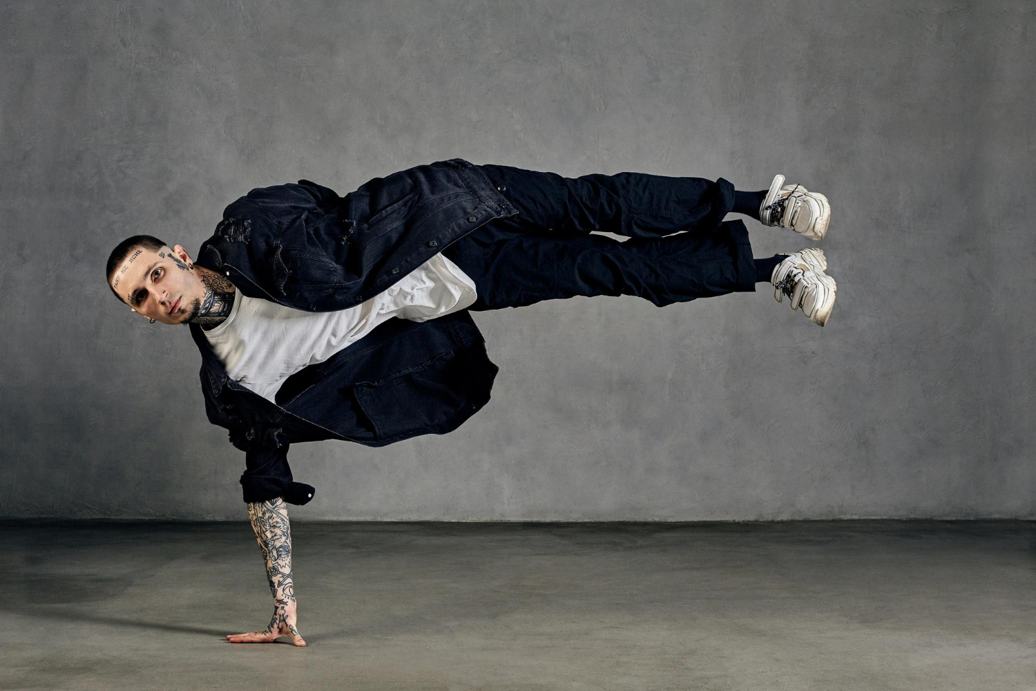 flexible fellow with tattooed body face earrings beard dressed white tshirt sneakers black denim shirt pants