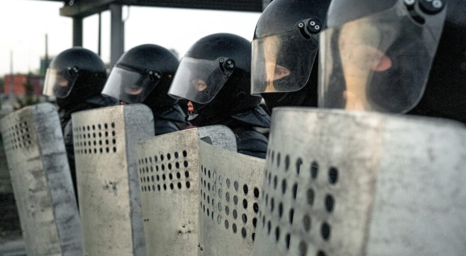 group of police squad in riot gear standing in a row holding shields while protecting against vaccine free protesters
