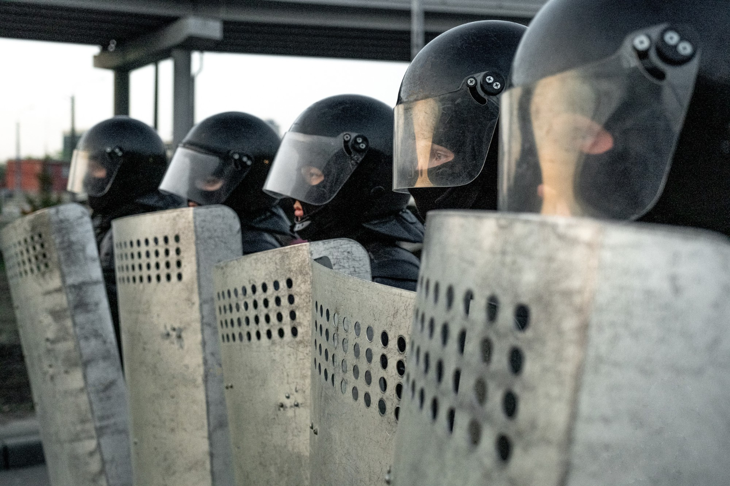 group of police squad in riot gear standing in a row holding shields while protecting against vaccine free protesters