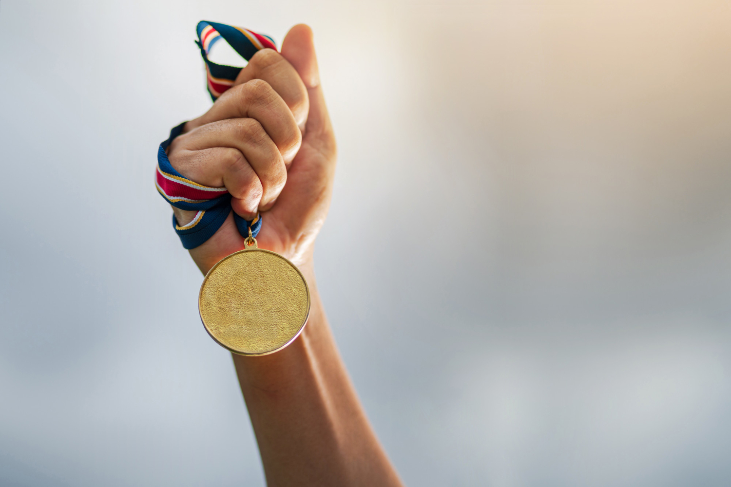 hand holding gold medal to the sky olympics