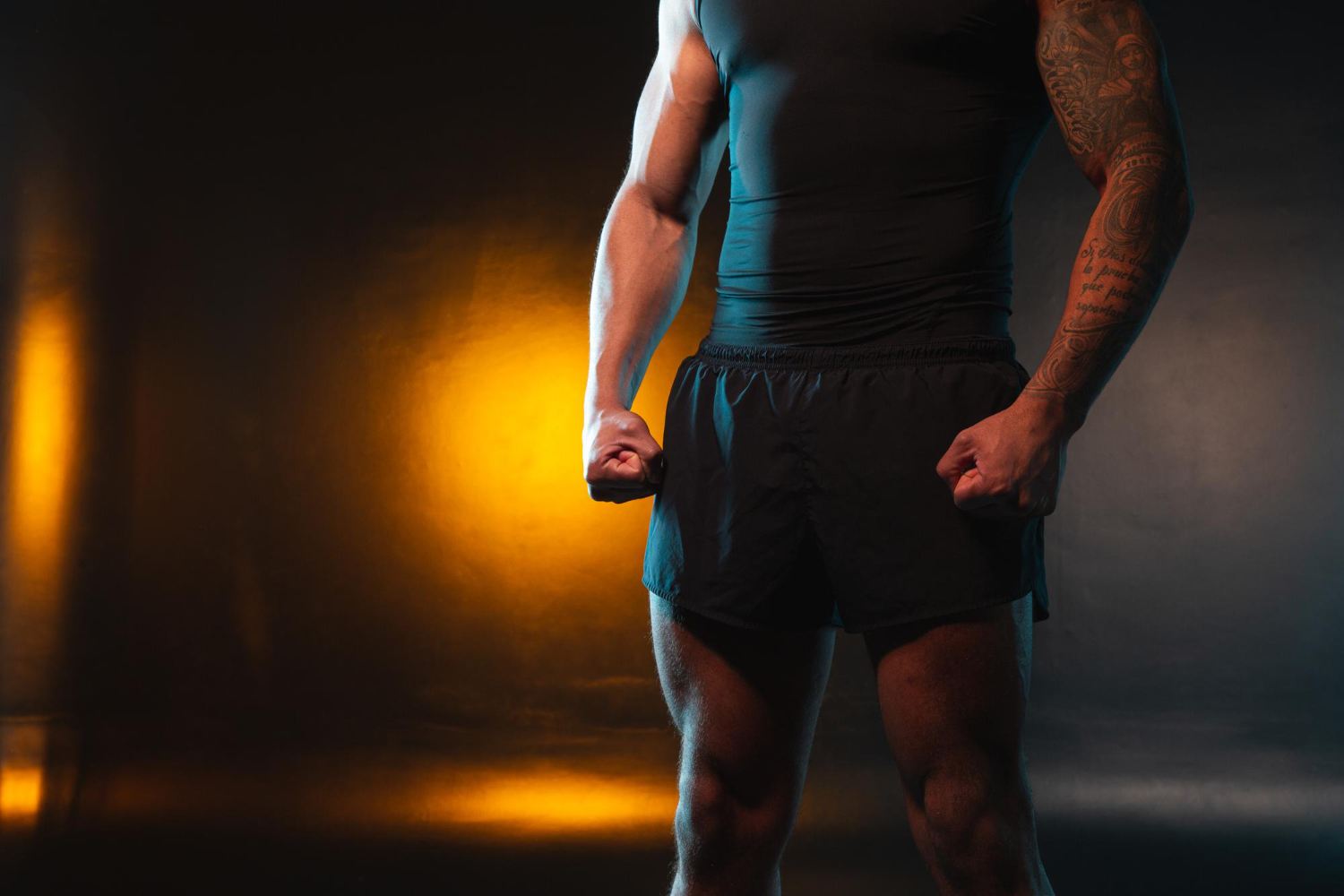 muscular man standing orange light background clenching fists