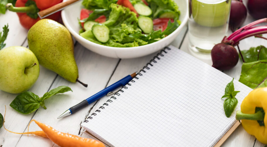 notepad with blank pages and bowl of fresh salad ingredients for a healthy clean food plan and healthy lifestyle