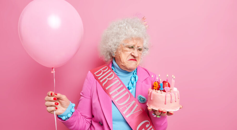old grey haired beautiful woman looks displeased birthday cake festive outfit holds inflated balloon