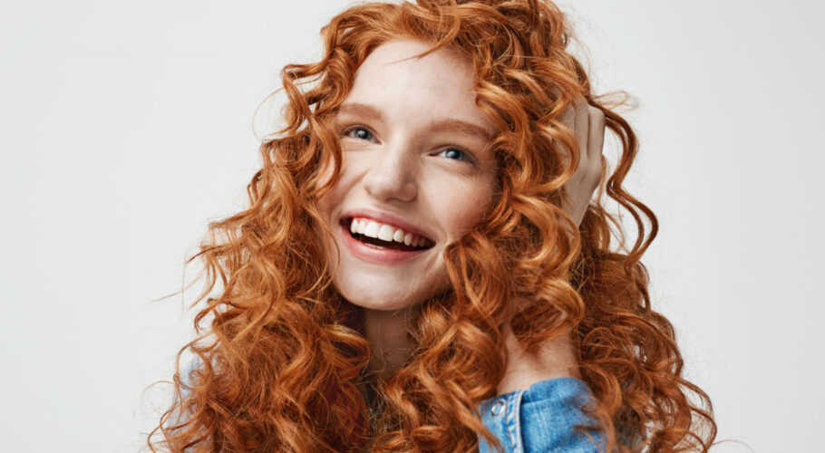 portrait cute happy girl smiling touching her curly red hair