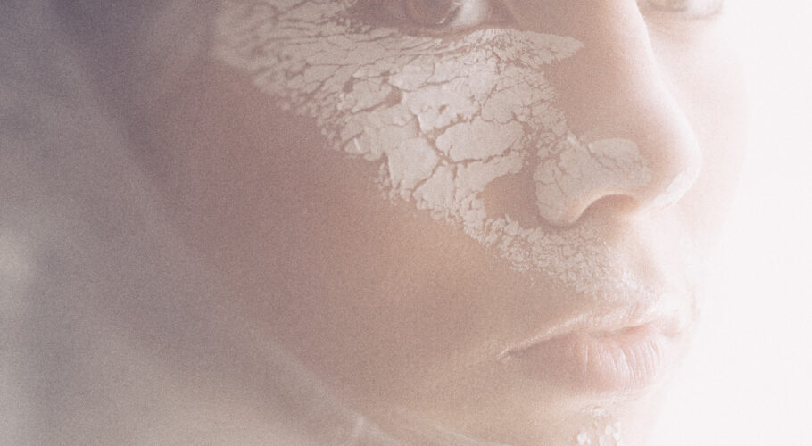 portrait of a woman's face with cracked white paint on her face in a white haze