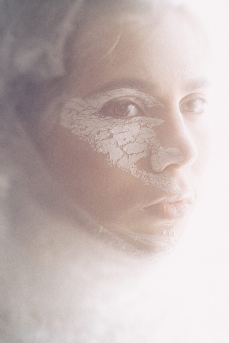 portrait of a woman's face with cracked white paint on her face in a white haze