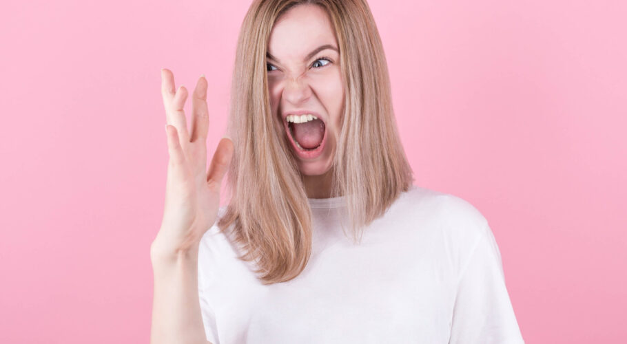 blonde woman screams in rage emotional and angry wearing white t shirt looking at her hand