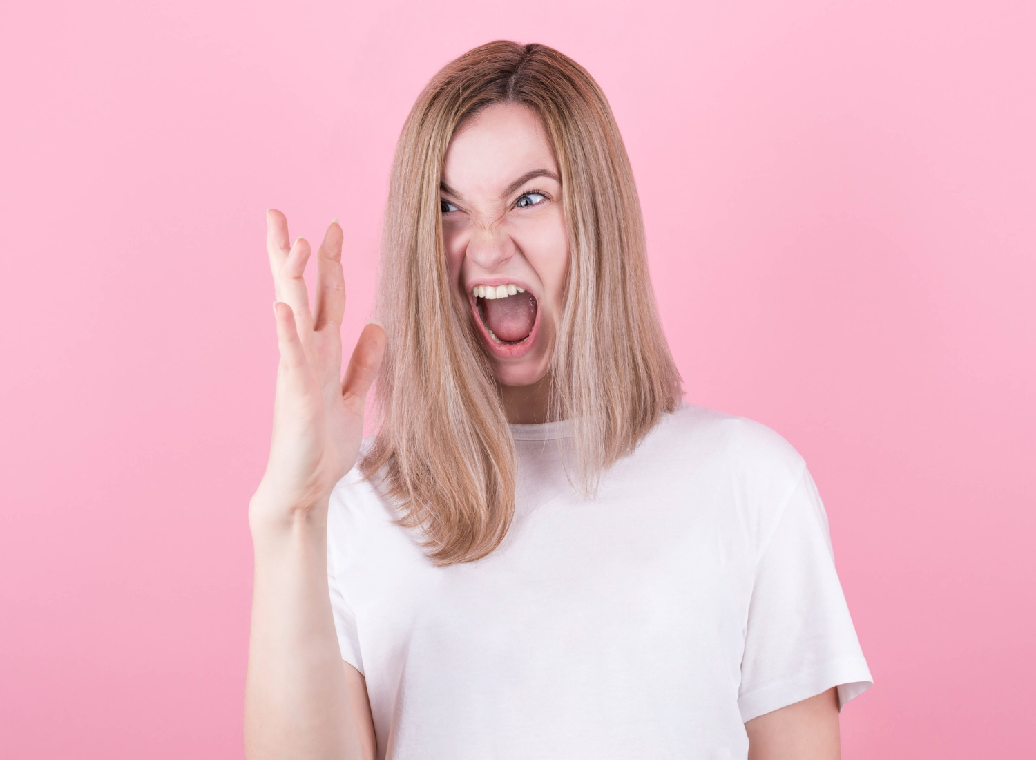 blonde woman screams in rage emotional and angry wearing white t shirt looking at her hand