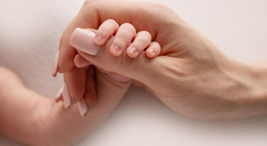 small hand with tiny fingers arm mother newborn baby holding finger parents after birth