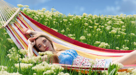 smiling woman sitting hammock among blooming yarrow