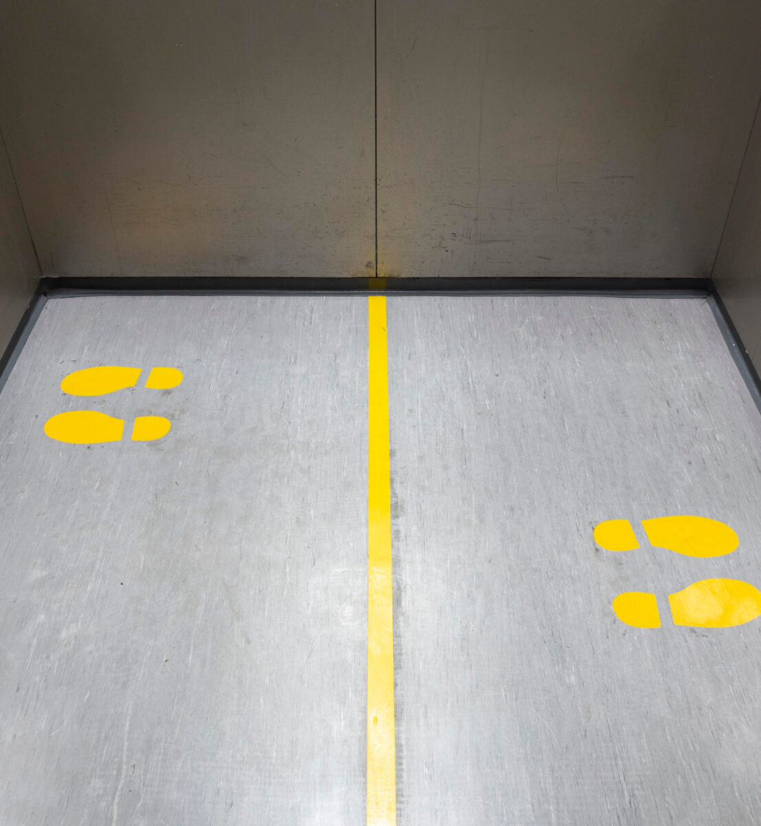 Socially Distancing Covid-19 With Yellow Footprings Inside Public Elevator