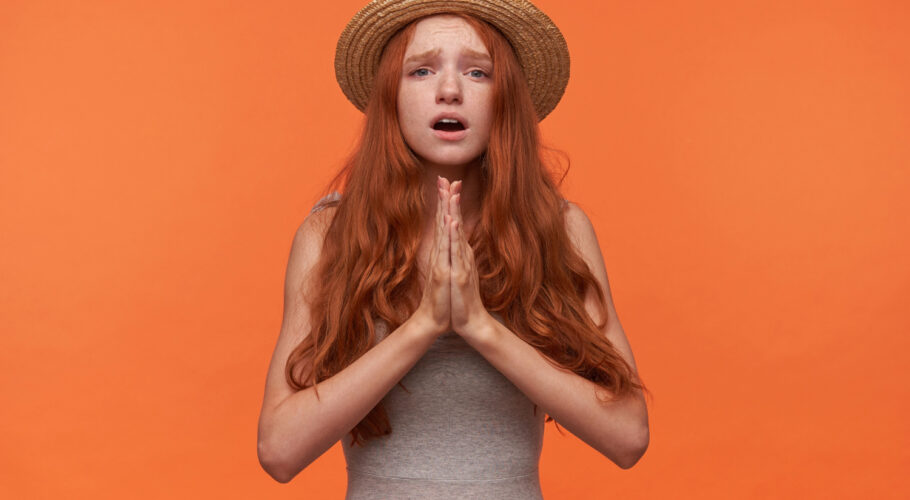upset young pretty woman with wavy red long hair standing orange
