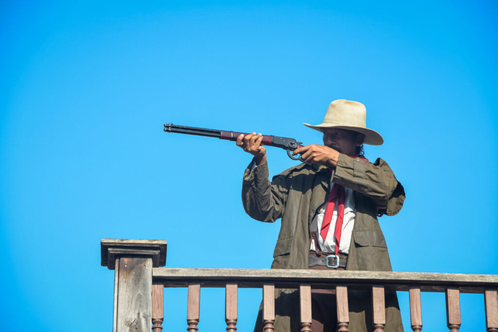 vintage cowboy holding rifle in his hand wearing a leather hat standing on a balcony focusing gun