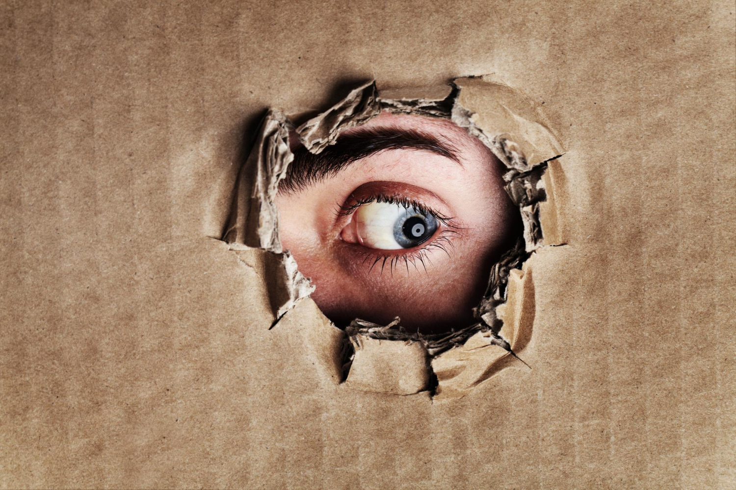 what is other side closeup anxiety depression panic portrait eye looking through ripped hole piece cardboard