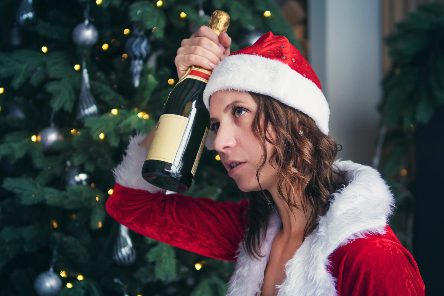 woman holding bottle champagne christmas tree hold his head headache from drinking alcohol hangover after holiday