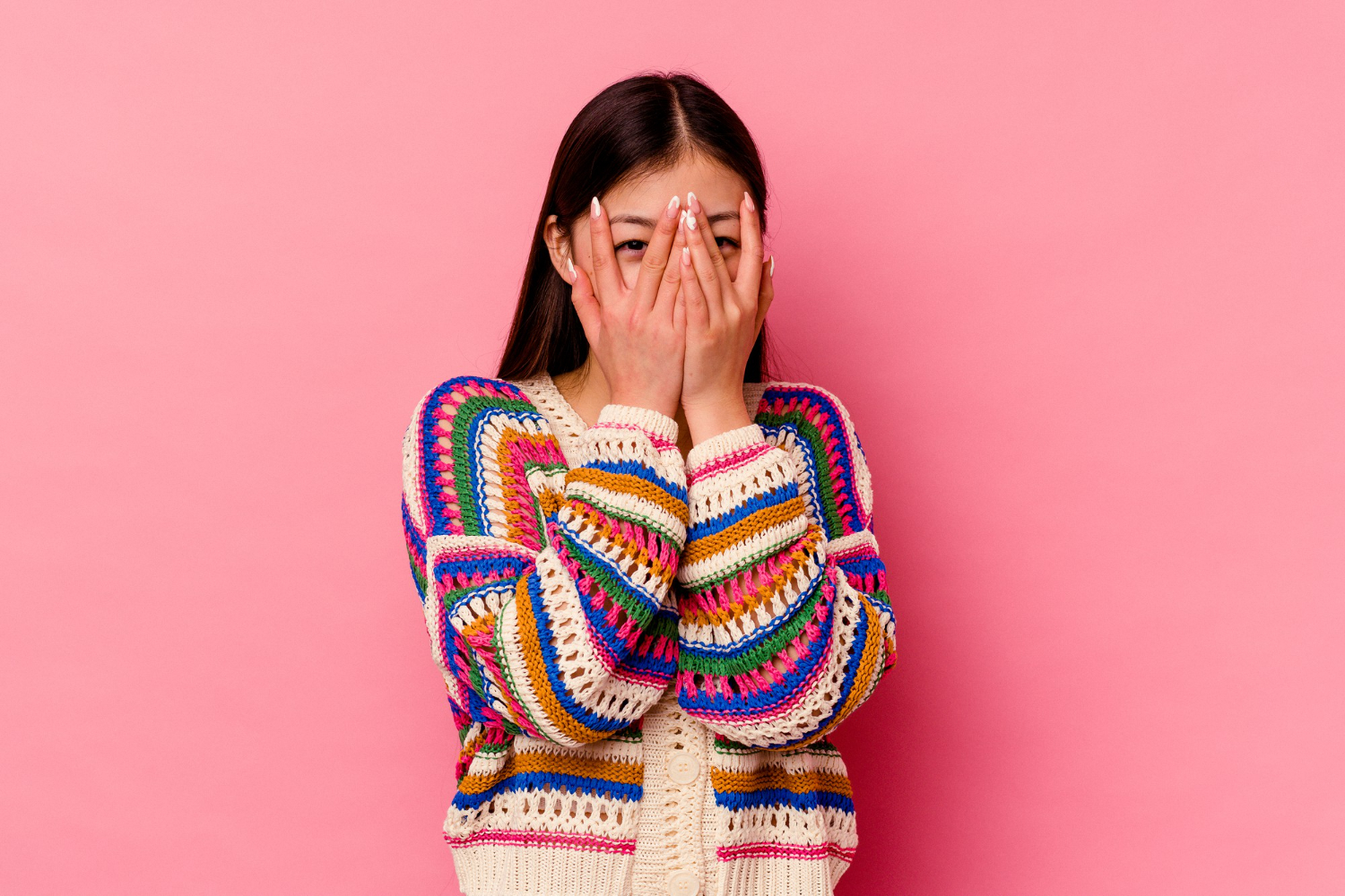 young chinese woman isolated pink wall blink through fingers embarrassed covering face