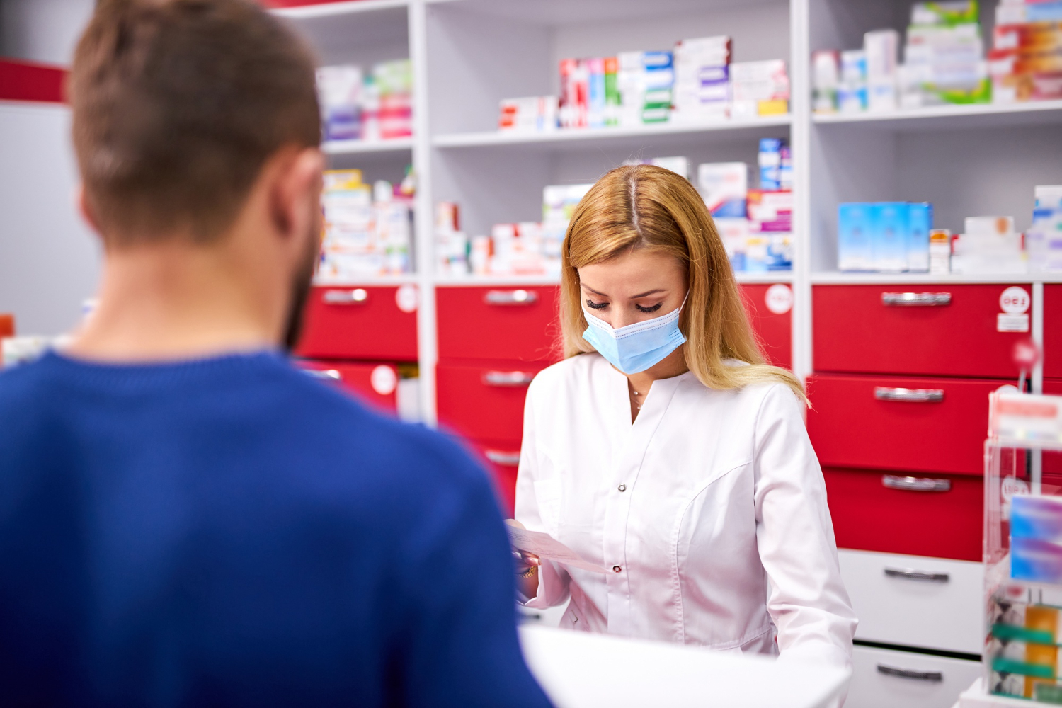 young female chemist cashier with protective medical face mask and young caucasian male customer buying drugs