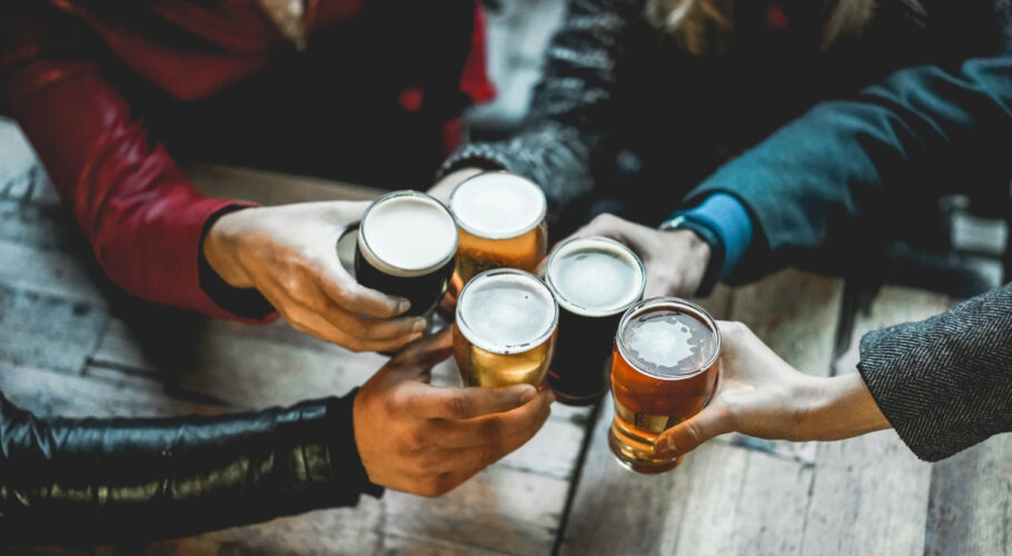young group of people having social drinks cheering with beer outdoors clasping glasses