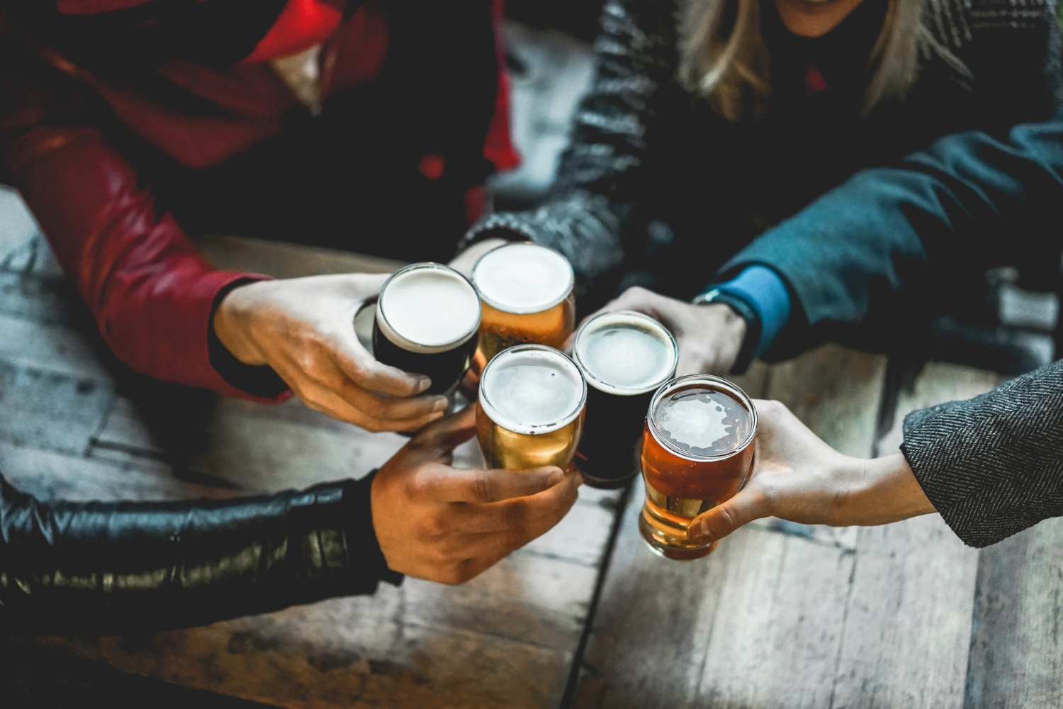 young group of people having social drinks cheering with beer outdoors clasping glasses