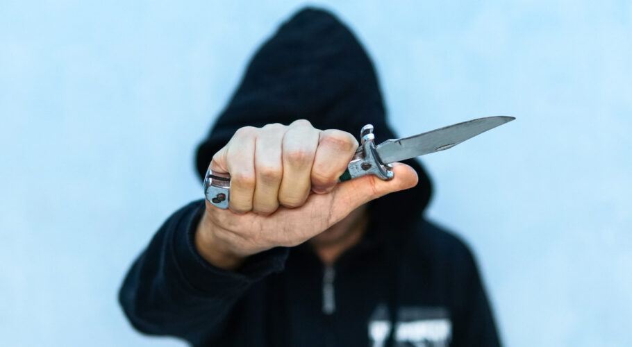 young man in hoodie holding a flick knife making threats
