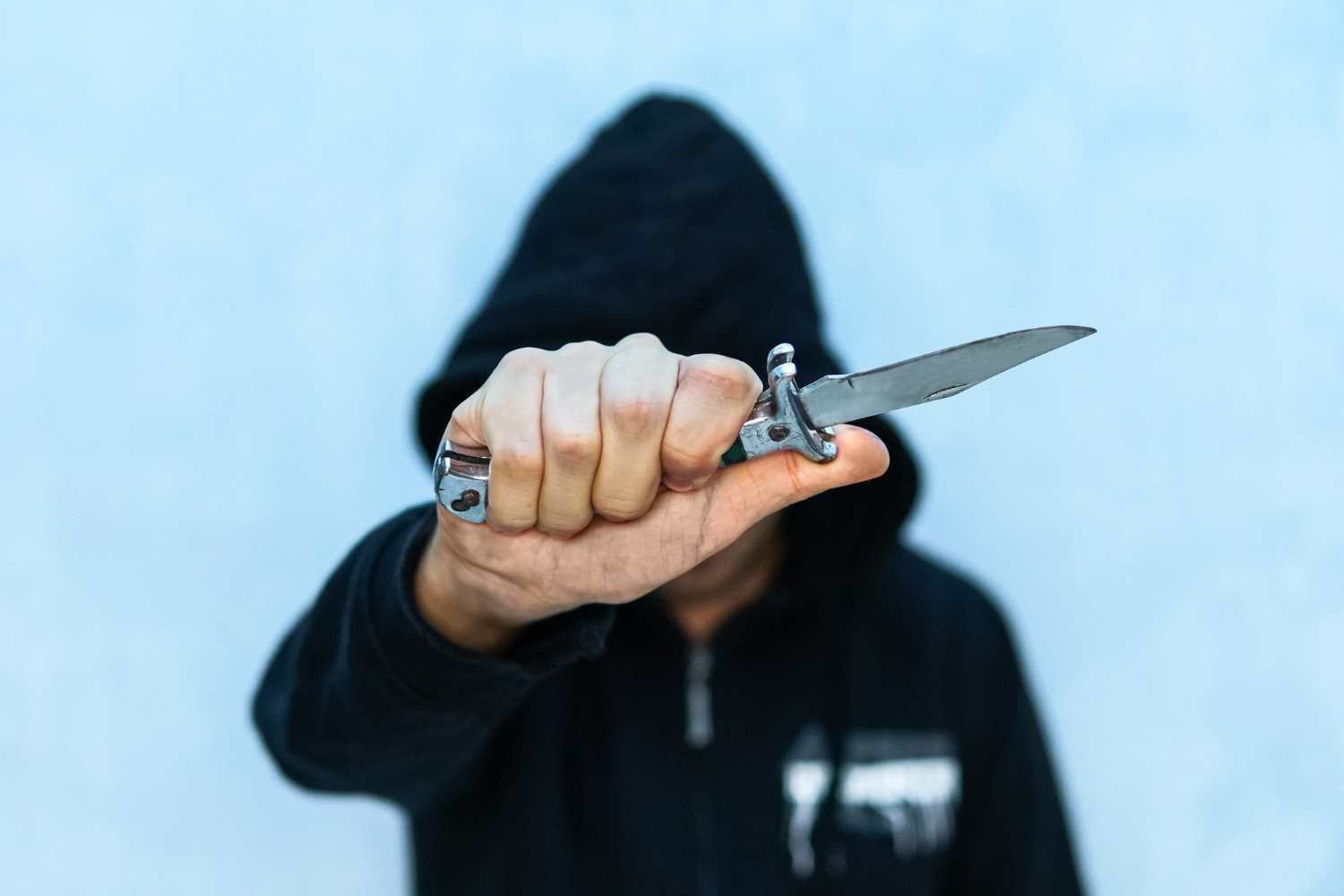 young man in hoodie holding a flick knife making threats