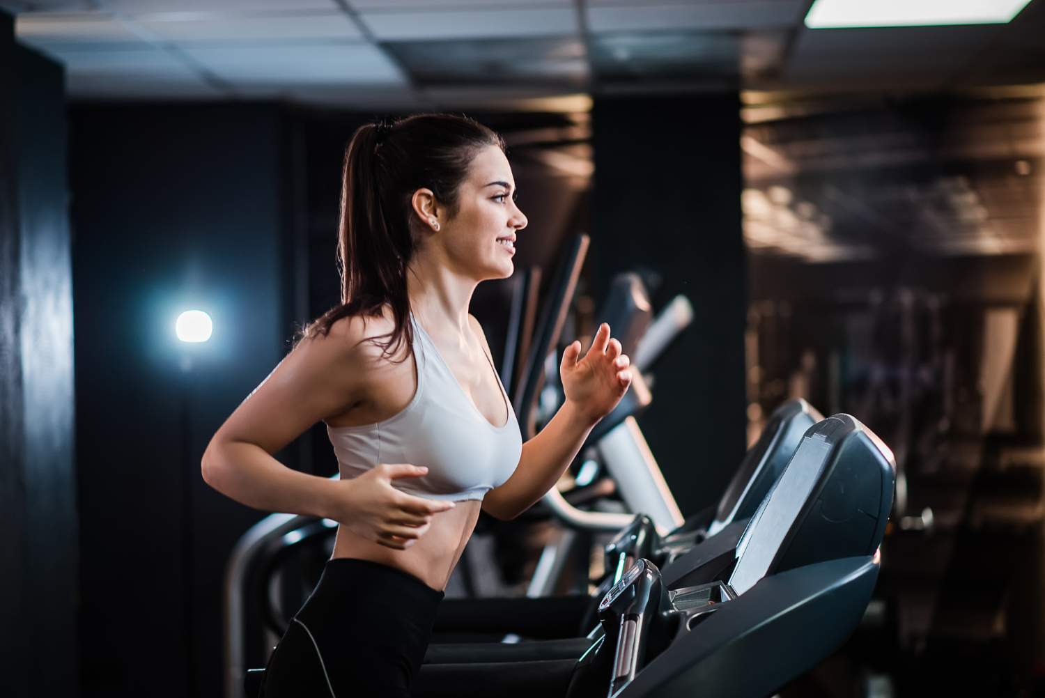 young sports woman with ponytail working out gym running treadmill side view