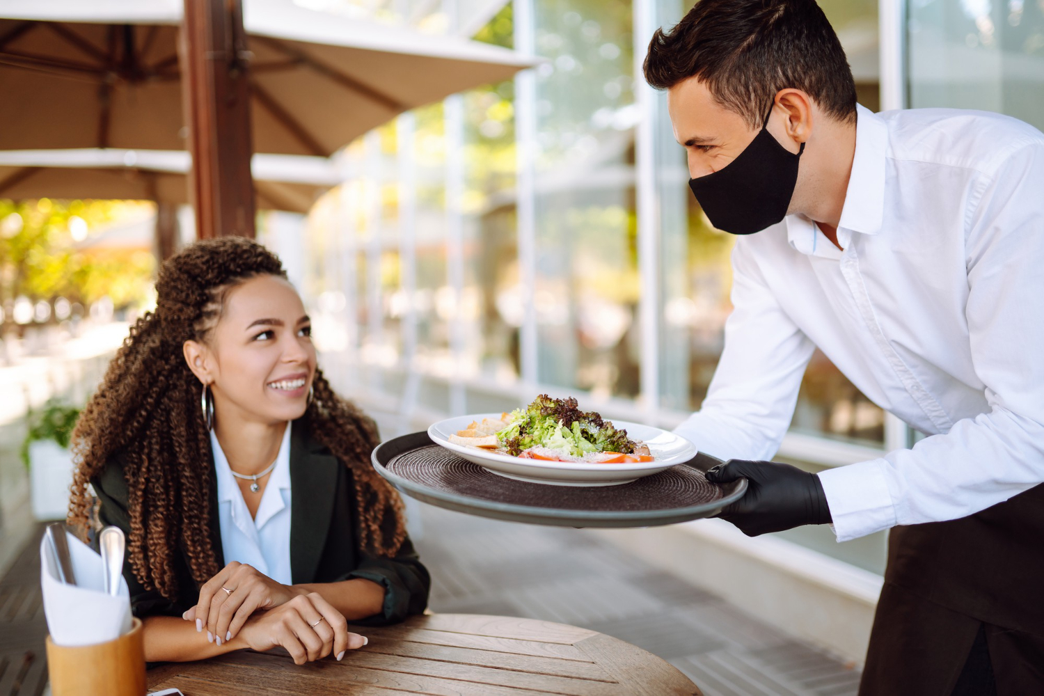 young waiter in a protective face mask wearing gloves with ordered meals ready to serve